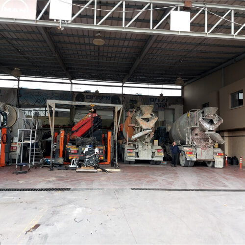 מרכז שירות מורשה למשאיות באשקלון - מבט מבחוץ למוסך שם עומדות משאיות שמקבלות שירות מימין לשמאל שני מערבלי בטון משאית על ליפט ועוד משאית